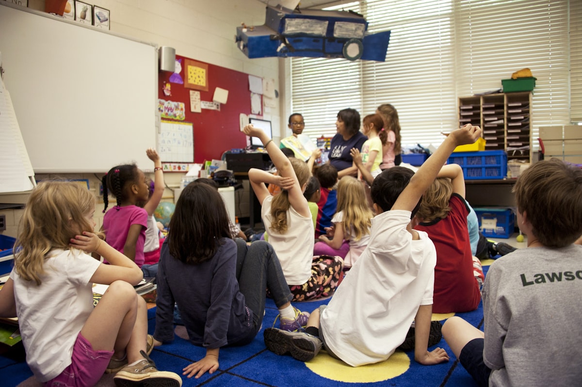 Diverse students raising hands in classroom