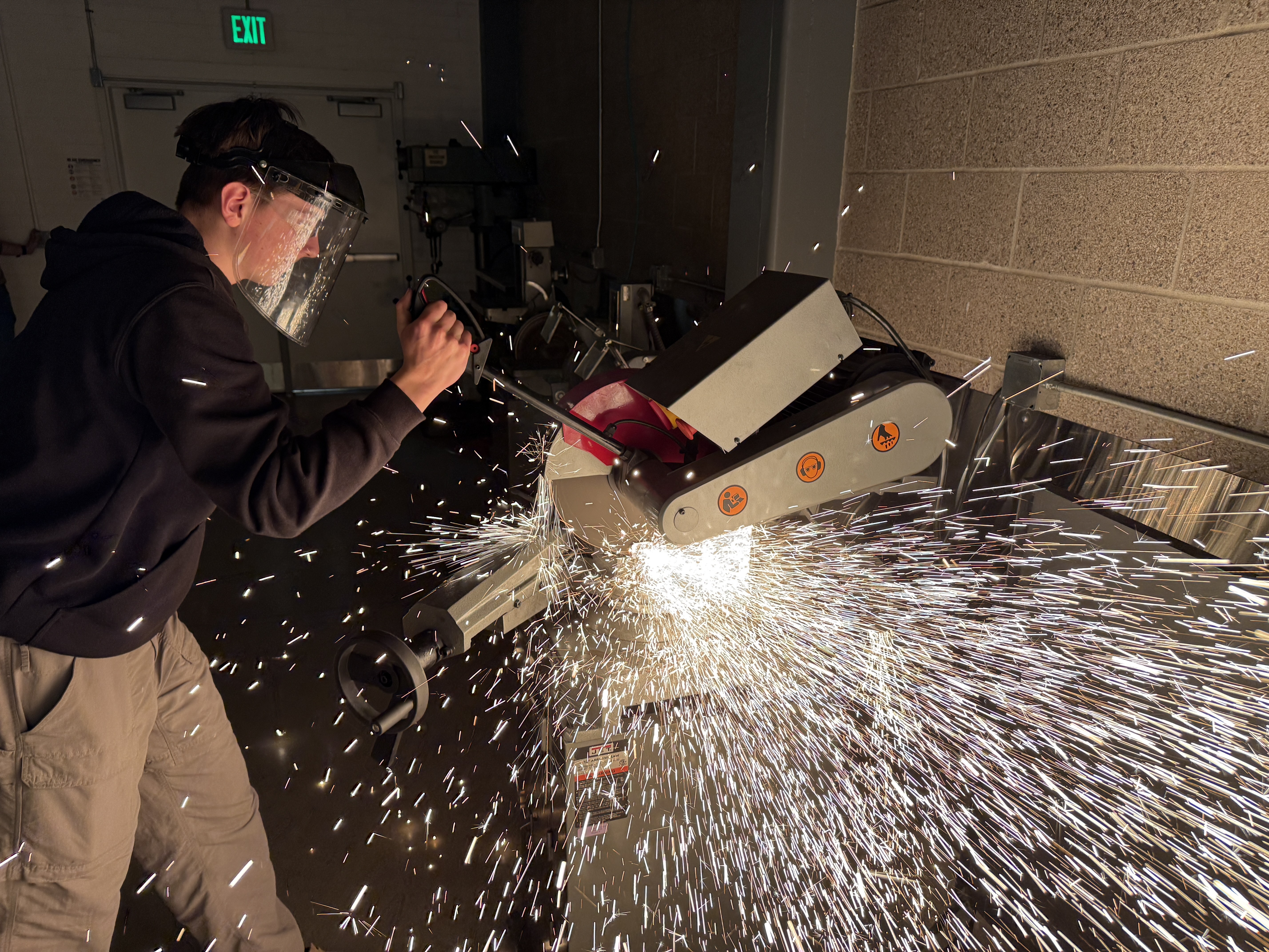 Student in face shield operating a chop saw with sparks flying