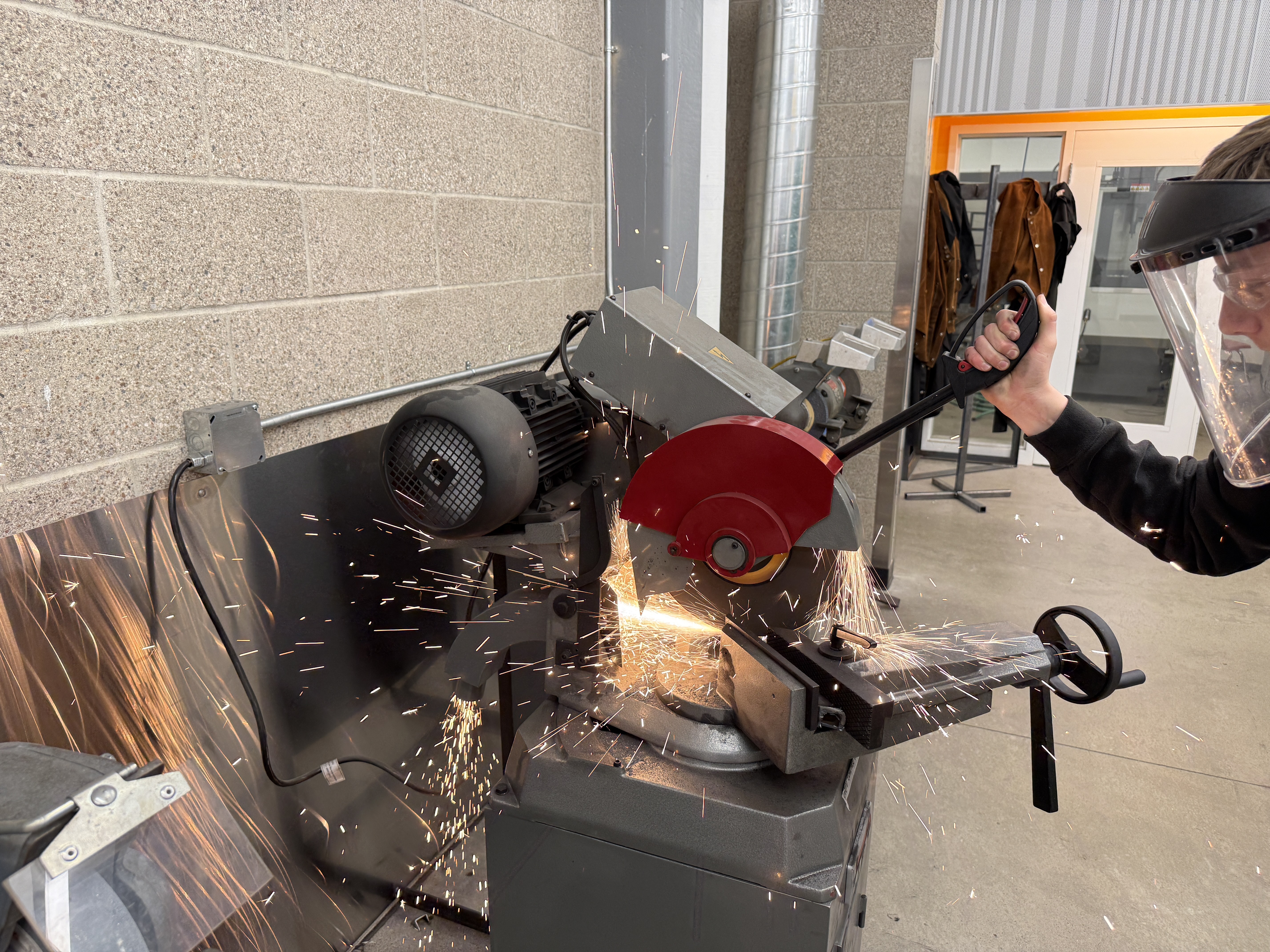 Student wearing face shield operating a metal cutoff saw