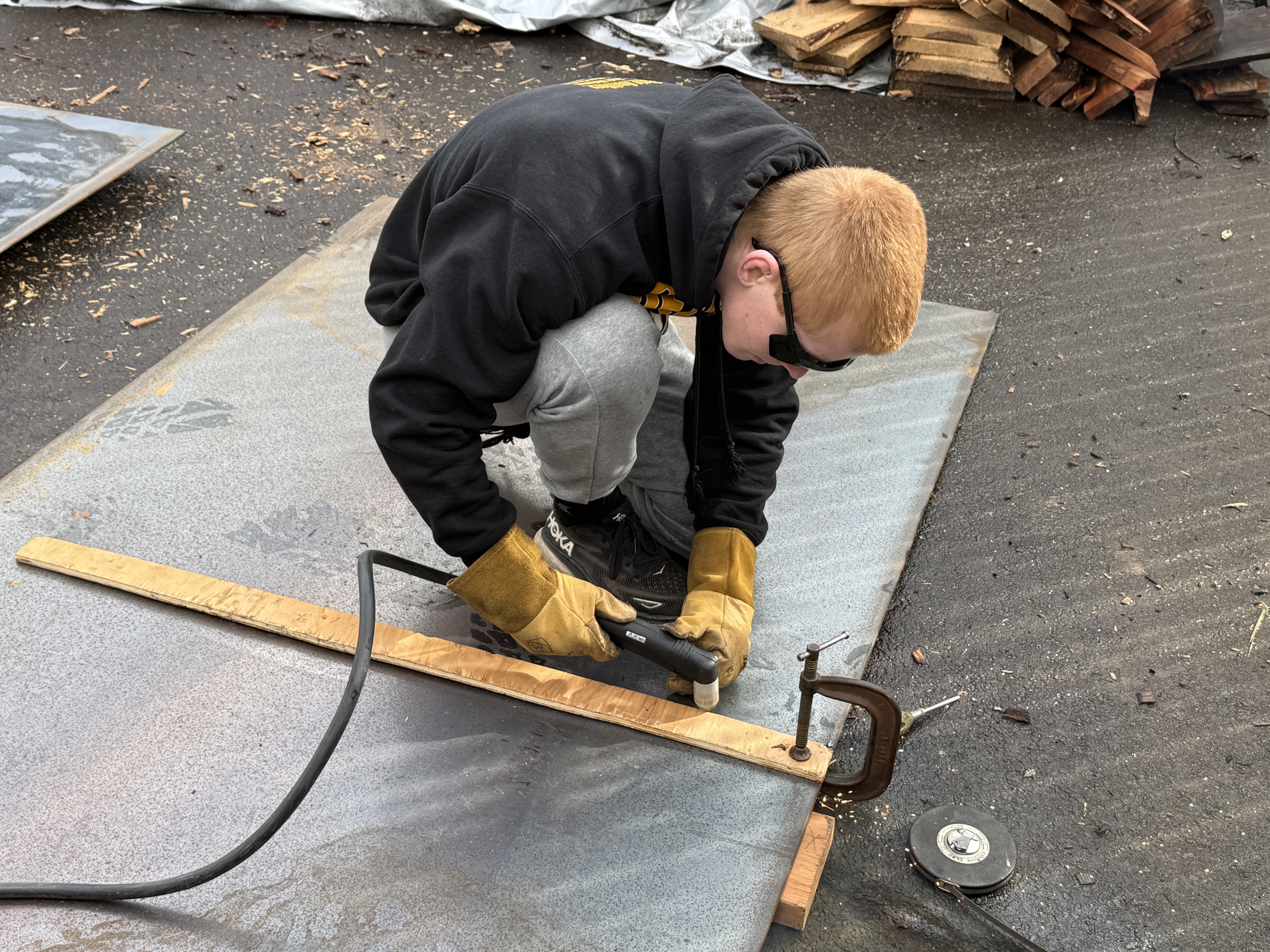 Student cutting a large sheet of metal outdoors