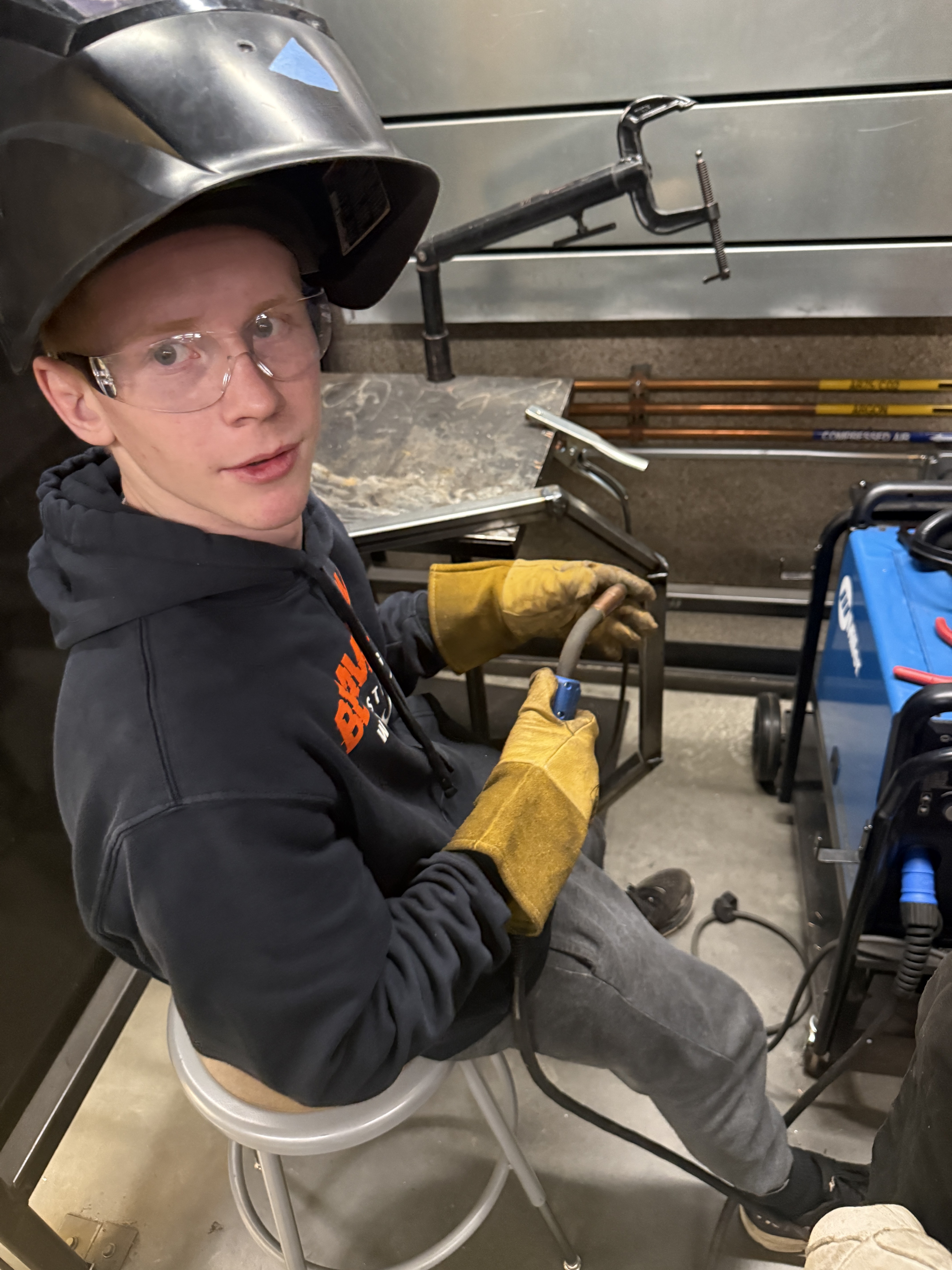 Student in welding helmet and gloves at a MIG welding station